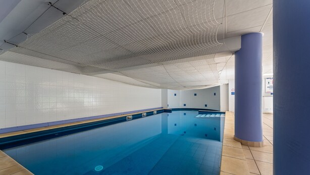 An indoor swimming pool with clear water, tiled walls, and a ceiling with a grid pattern. - La Parenthèse d'Uzès - Avec Parking Privé (Uzes)