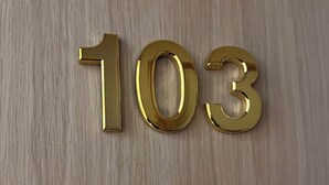 Kolme kullanväristä numeroa – ’1’, ’0’ ja ’3’ – on sijoitettu puupinnalle.