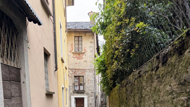 A narrow cobblestone alley with buildings on either side, a stone wall on the right, and a wooden door at the end. - Ca'Lina by Lago Maggiore Rentals & Estate (Cannobio)