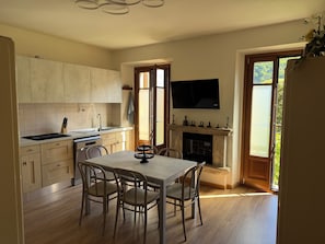 Eine moderne Küche mit Holzausstattung, einem Esstisch mit Stühlen, einem Kamin und einem darüber montierten Fernseher.