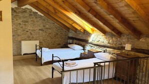 An attic bedroom with two beds, stone walls, wooden beams, and a metal railing. - Ca'Lina by Lago Maggiore Rentals & Estate (Cannobio)