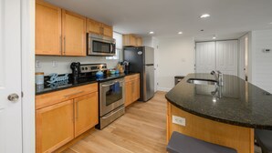 A modern kitchen with wooden cabinets, stainless steel appliances, and a granite countertop. - Newly Renovated Opal Condo Dewey's Best Location (Dewey Beach)