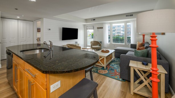 A modern kitchen with a large island, a dining area with a sofa and chairs, and a living room with a TV. - Newly Renovated Opal Condo Dewey's Best Location (Dewey Beach)