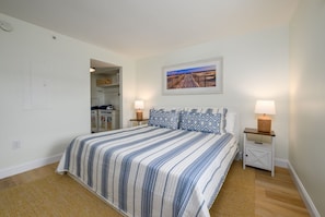 Une chambre à coucher avec un lit, deux tables de chevet, une commode, un tableau accroché au mur et une porte donnant sur une salle de bain.