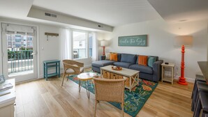 A living room with a sofa, a table, a chair, a lamp, and a view through a door. - Newly Renovated Opal Condo Dewey's Best Location (Dewey Beach)