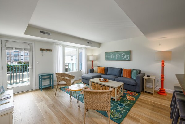 Un salon avec un canapé, une table, une chaise, une lampe et une vue sur l’extérieur, visible à travers une porte.