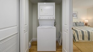 A laundry room with a front-loading washer and dryer, a bed with striped bedding, and a framed picture on the wall. - Newly Renovated Opal Condo Dewey's Best Location (Dewey Beach)