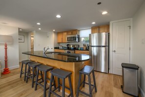 Une cuisine moderne dotée d’un îlot central, de tabourets de bar, d’appareils électroménagers en acier inoxydable et d’armoires en bois.