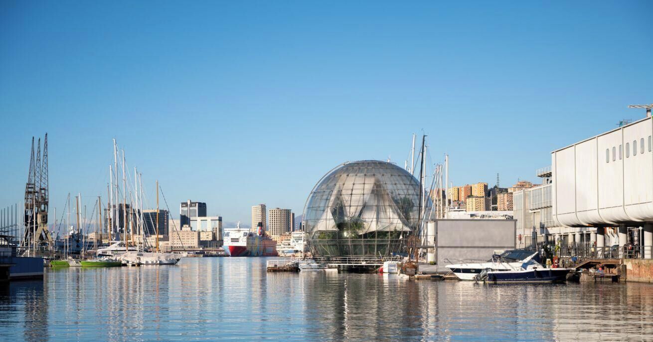 Un port de plaisance avec des bateaux, une grande structure en forme de dôme transparent et, au fond, des bâtiments industriels.