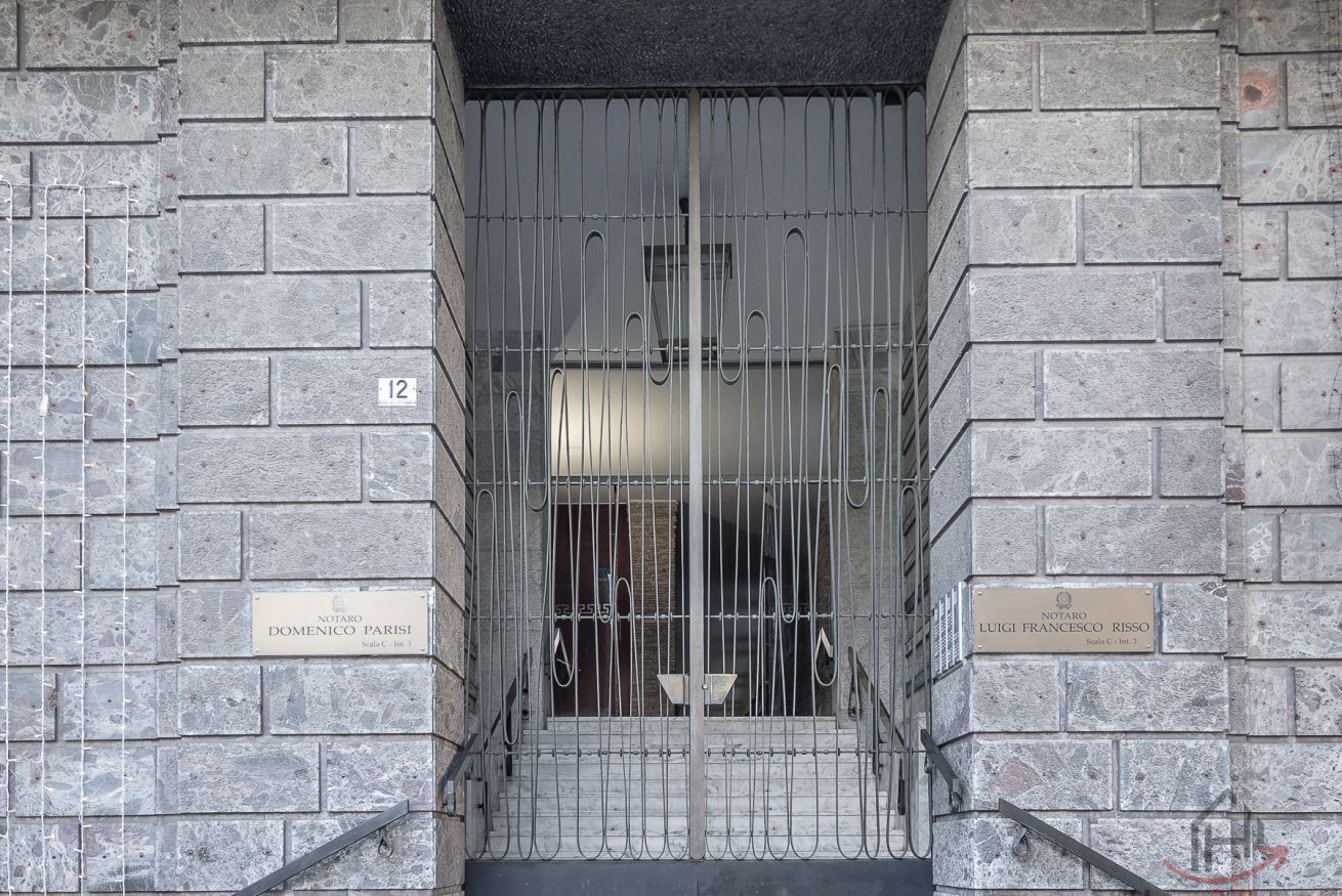 Une entrée fermée par un portail, agrémentée de deux plaques commémoratives, l’une dédiée à Domenico Parisi et l’autre à Luigi Francesco Rissio, ainsi que le chiffre « 12 » peint sur le mur.