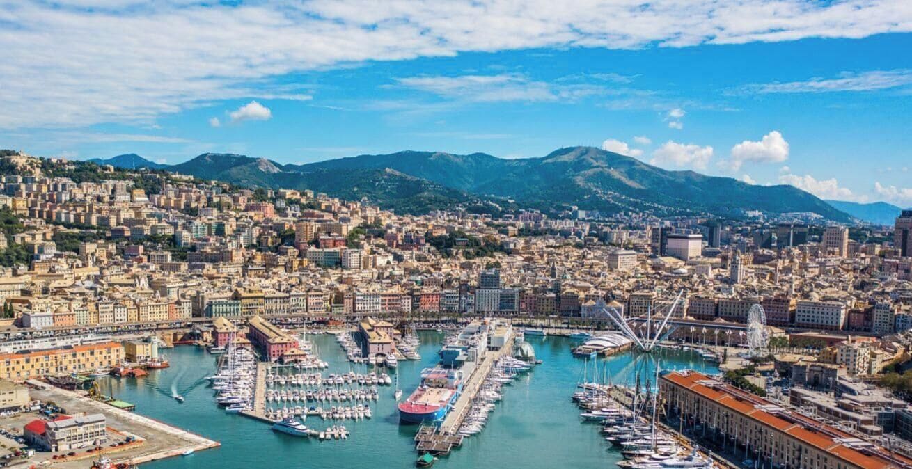 Un paysage urbain côtier avec un port de plaisance, des bâtiments et des montagnes en arrière-plan.