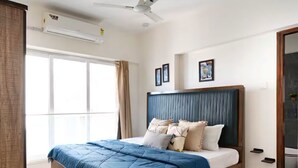 Ein Schlafzimmer mit Bett, Deckenventilator, Klimaanlage und einem Fenster mit Vorhängen.