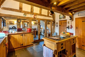 Eine rustikale Küche mit Holzbalken, Steinböden und einer Holzinsel mit einem roten Wasserkocher.