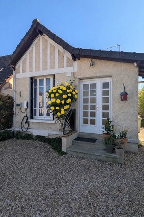 Ein Haus mit weißer Tür, einem Fenster mit weißem Rahmen, einer kleinen Veranda und einem Schotterweg.