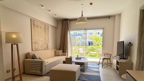 A modern living room with a sofa, ottoman, coffee table, lamp, TV, and a view of the outside. - Fouka North Coast SA-9B-G02 (Marsa Matrouh)