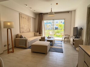 A modern living room with a sofa, ottoman, coffee table, lamp, TV, and a view of the outside. - Fouka North Coast SA-9B-G02 (Marsa Matrouh)