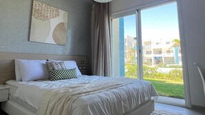 A hotel room with a bed, a ceiling fan, a large window, and a view of the outside. - Fouka North Coast SA-9B-G02 (Marsa Matrouh)