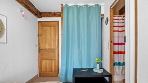 Ein Zimmer mit Holztür, blauem Vorhang, einem kleinen Tisch mit einer Vase und einem gestreiften Duschvorhang.