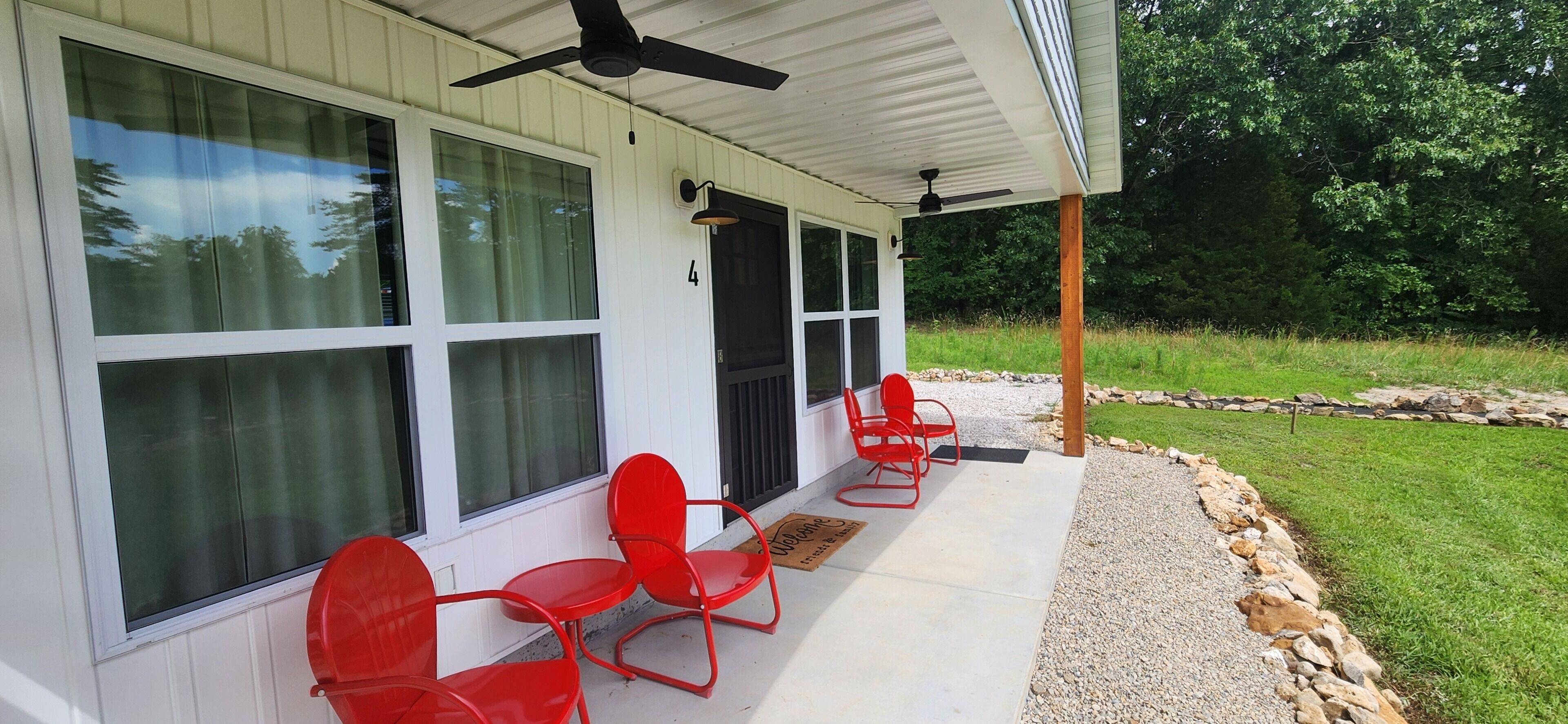 A covered porch with large windows, a ceiling fan, and red chairs.