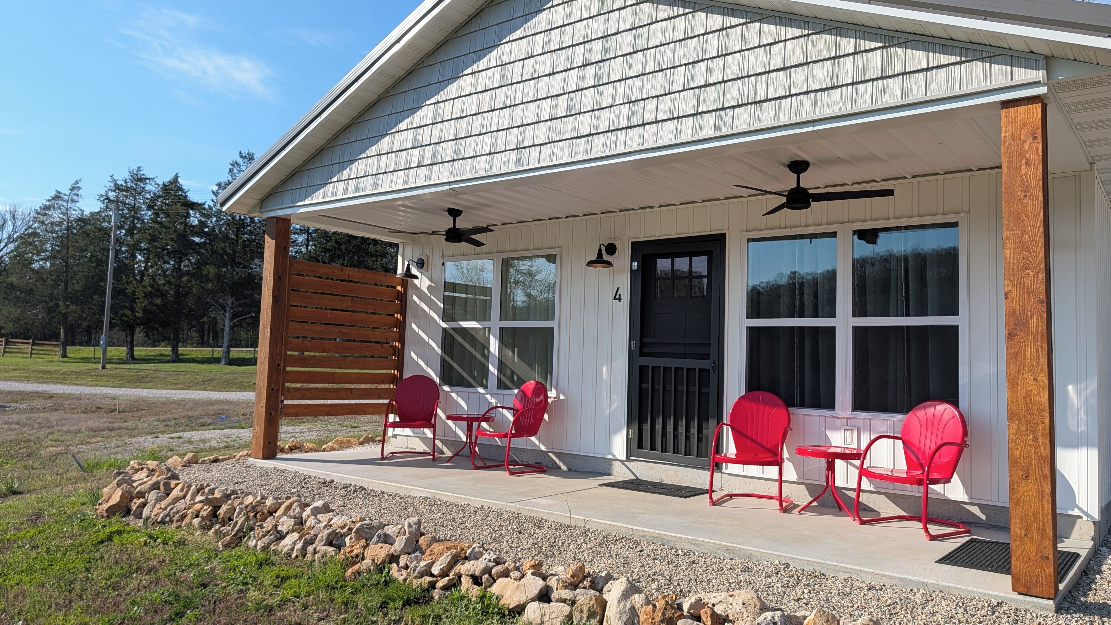 A building with a covered porch, red chairs, and a ceiling fan.