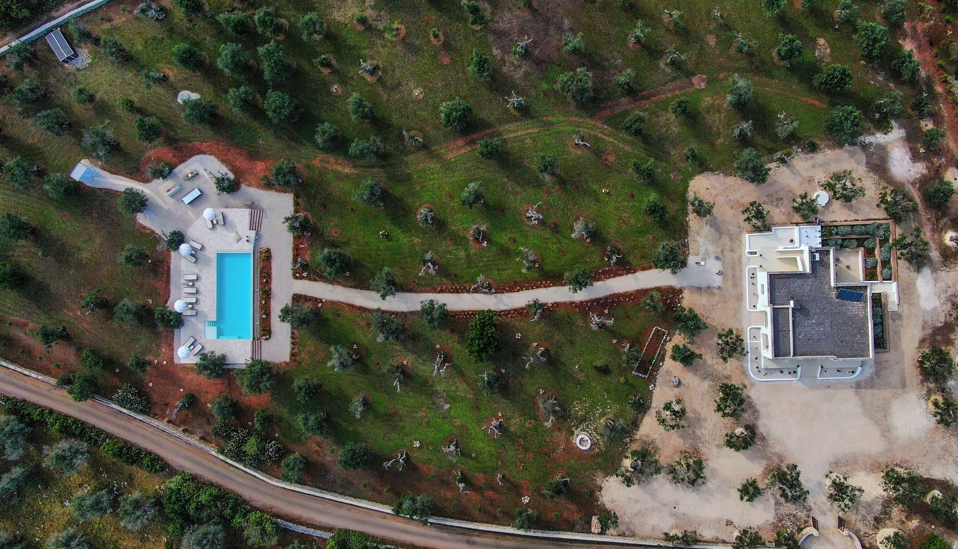 Vue aérienne d’une propriété comprenant une piscine, un grand bâtiment et un jardin aménagé.