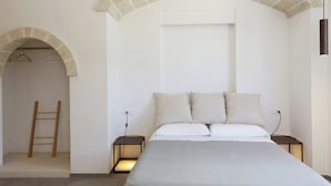 Ein Schlafzimmer mit einem Bett, zwei Nachttischen, einer Treppe aus Holz und einem Steingewölbe.