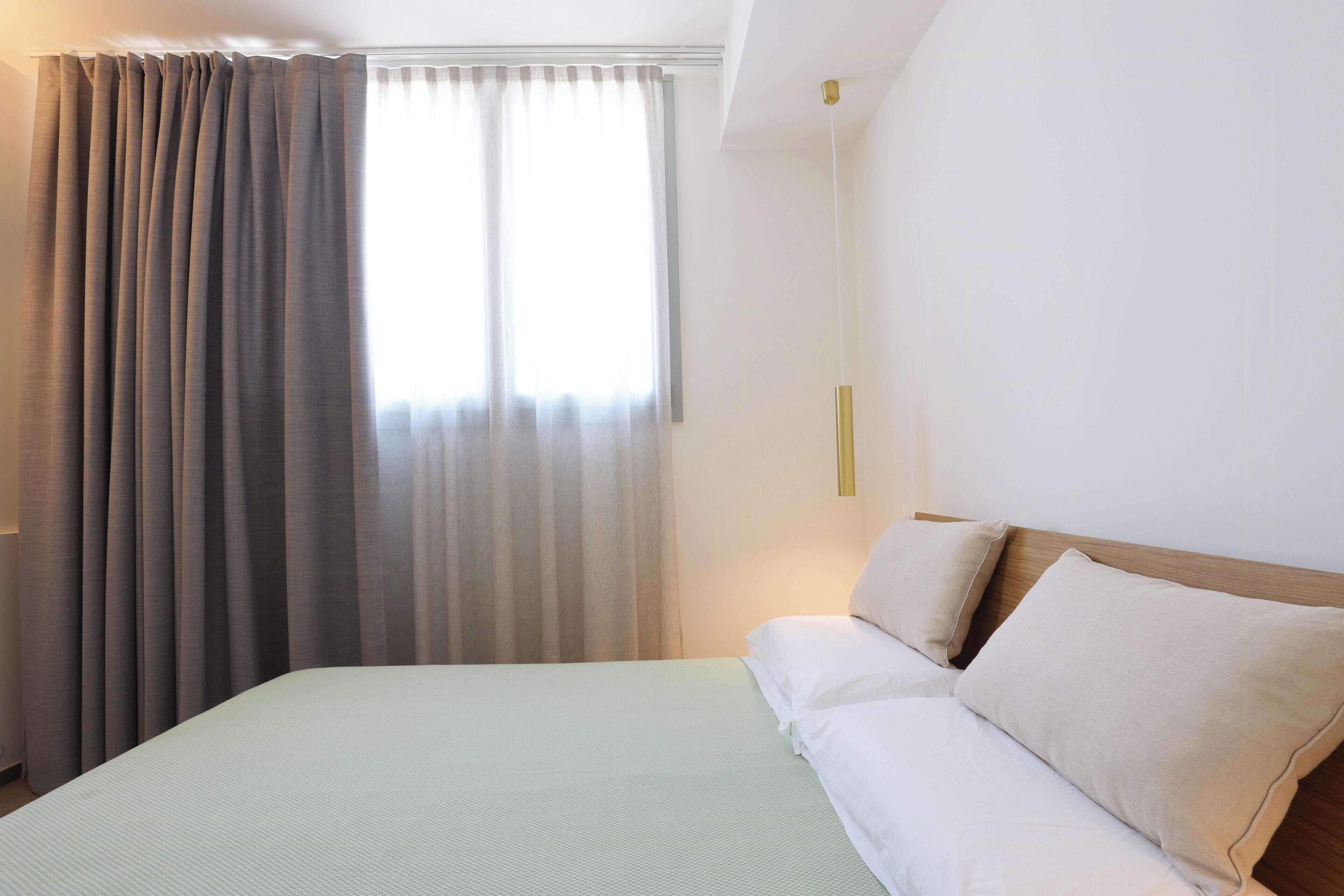 Ein Hotelzimmer mit Bett, Vorhängen, einem Nachttisch und einer Wandleuchte.