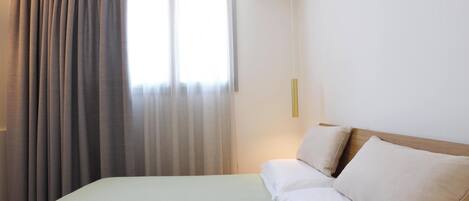 Habitación de hotel con cama, cortinas, mesita de noche y lámpara de pared.