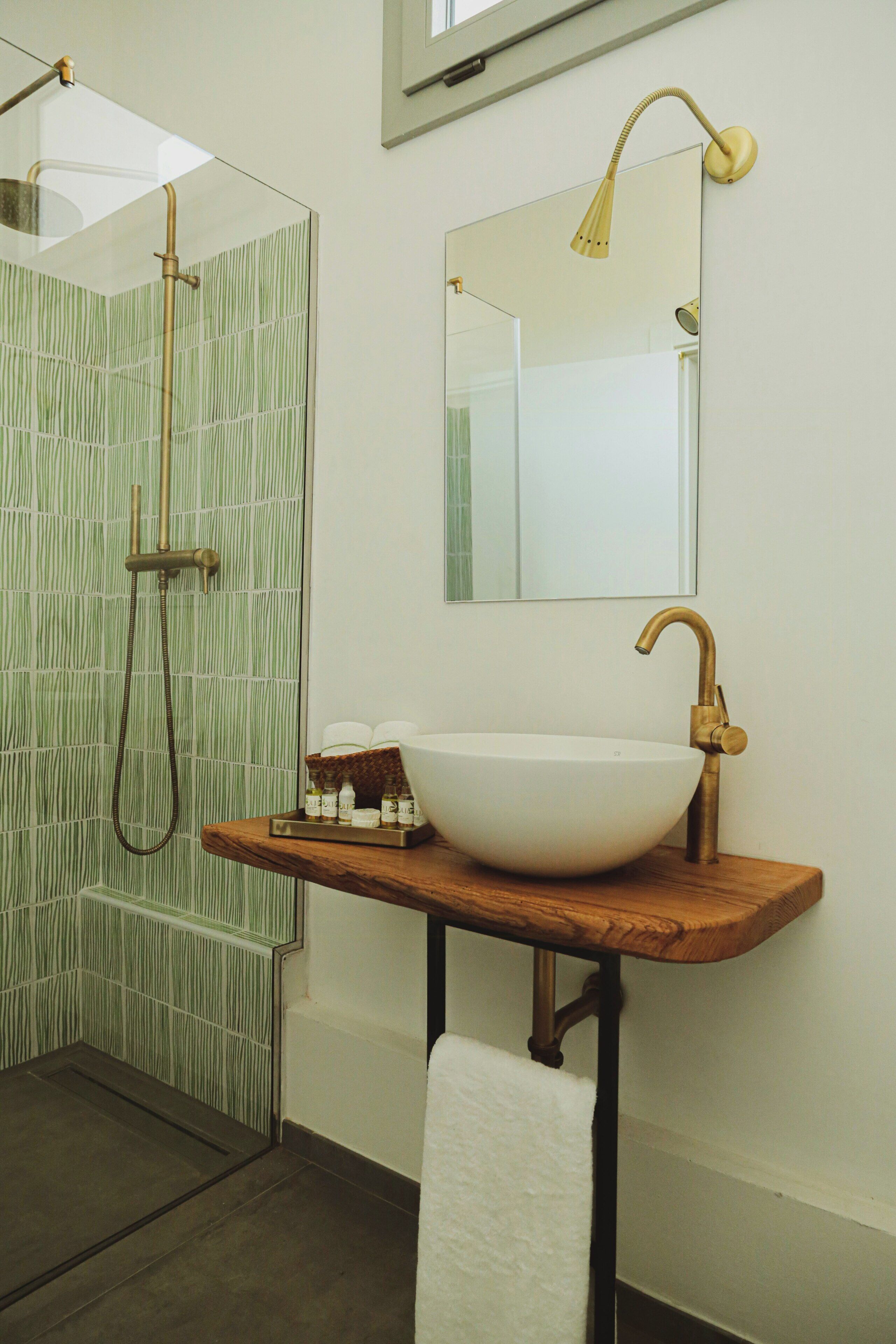 A bathroom with a glass shower enclosure, a white sink with a wooden countertop, and a mirror above the sink.