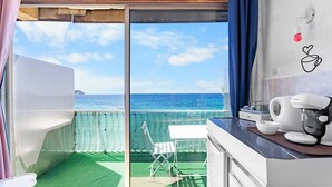 A balcony with a view of the sea, a white table, a chair, a coffee maker, and a wall art piece. - Studio “Jeux de boules 5” with sea view (Le Pradet)