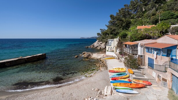 A coastal scene with clear blue water, a rocky beach, and colorful kayaks lined up on the shore.