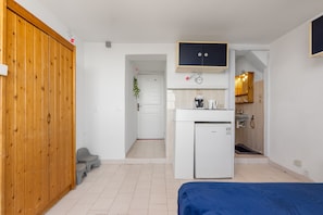 Ein gemütlicher Raum mit Holzschrank, einer kleinen Küchenzeile, einem Bett und einem Badezimmer.