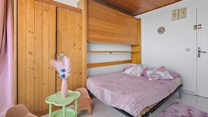 A bedroom with a bed, a wooden wardrobe, a small table, and a chair.