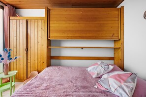A bedroom with a bed, a wooden wardrobe, a green chair, and a vase with flowers. - Studio "Porte Rouge 5" with Sea View (Le Pradet)