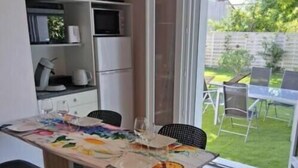 A dining area with a table set for four, chairs, a television above the table, and a sliding glass door leading to an outdoor patio. - Charming apartment with swimming pool 6 km from the Vendée beaches (Notre-Dame-de-Riez)