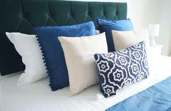A bed with a tufted headboard, white bedding, and four decorative pillows in various patterns and colors. - The Emerald Bloom, 2BHK Apt near Airport,Bkc&NMACC (Mumbai)