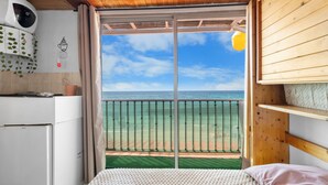 Ein Schlafzimmer mit Balkon und Meerblick, einem Bett, einem weißen Kühlschrank und einer Holzbalkendecke.