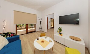 A modern living room with a sofa, a coffee table, a TV, and a sliding glass door leading to a garden. - Al Pino Blue house by Istra Vacation (Premantura)