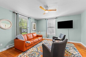 A living room with a sofa, chairs, a television, and a ceiling fan.