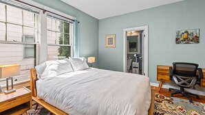 A bedroom with a bed, bedside table, lamp, chair, desk, and a window with blinds. - Centrally Located in Brownes Addition (Spokane)