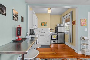 A compact kitchen with white cabinets, a stove, microwave, and a dining area with a bar stool.
