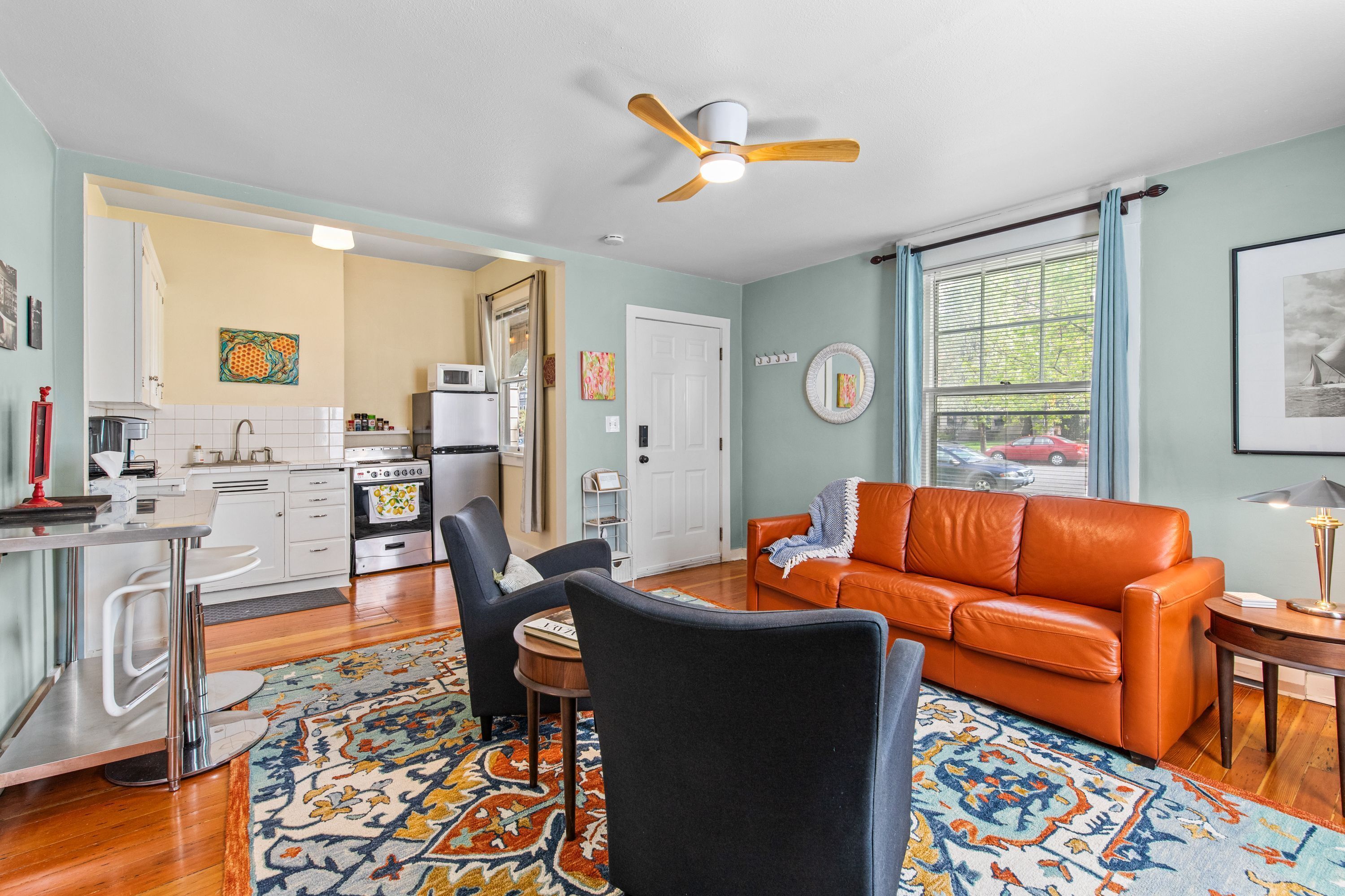 A living room with a sofa, chairs, a dining table, and a kitchen in the background.