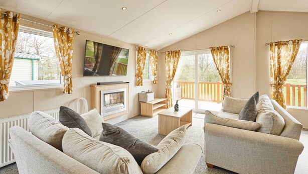 Ein Wohnzimmer mit Kamin, Sofa, Fernseher und großen Fenstern mit Vorhängen.