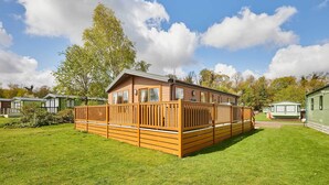 Eine Holzhütte mit umzäunter Terrasse, umgeben von einem gepflegten Rasen.