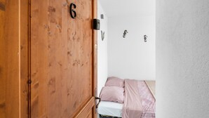 A wooden door with the number 6, a bed with pink bedding, and a white wall with a small picture. - Studio "Porte Rouge 6" with Sea View (Le Pradet)