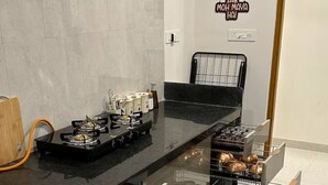 A kitchen with a gas stove, a microwave, and a built-in oven. There are cabinets below the counter and a wall-mounted rack. - URBAN PAUSE, 2BHK Apt near BKC,airport&NMACC (Mumbai)