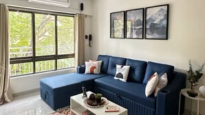 A modern living room with a blue sectional sofa, a white coffee table, and a patterned rug. - URBAN PAUSE, 2BHK Apt near BKC,airport&NMACC (Mumbai)