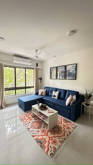 Ein modernes Wohnzimmer mit einem blauen Ecksofa, einem weißen Couchtisch und einem gemusterten Teppich.