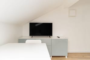 Una camera moderna con una TV a schermo piatto montata su un mobile chiaro, un tavolo bianco e una sedia bianca.