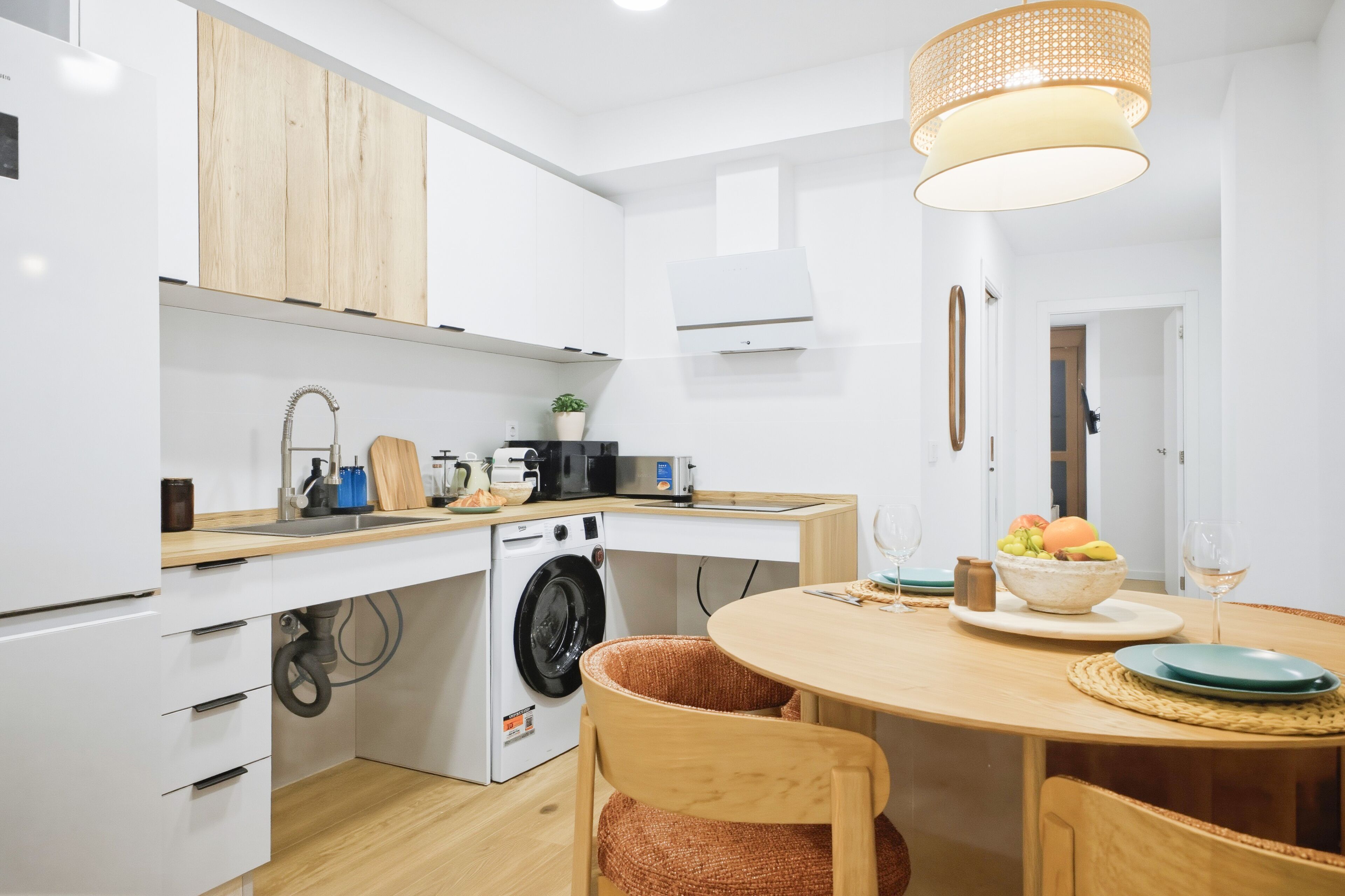 Una cocina moderna con lavadora integrada, un comedor con una mesa redonda y una lámpara colgante.